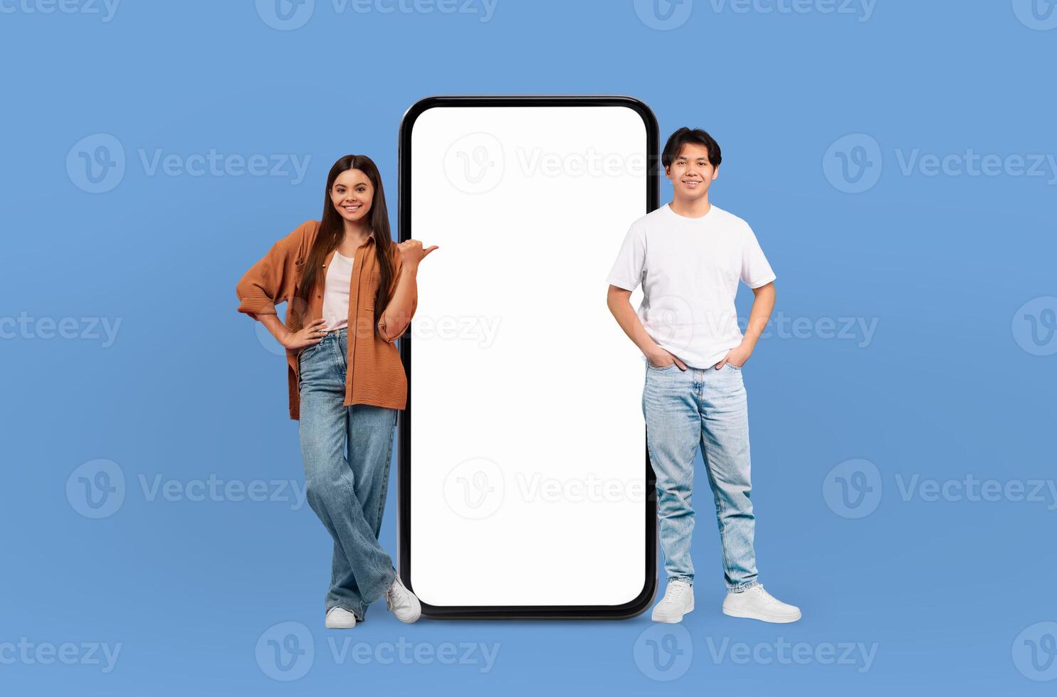 With joyful faces, the young multiracial man and woman pose beside a blank-screened, life-sized smartphone, emphasizing the endless possibilities for customization. photo
