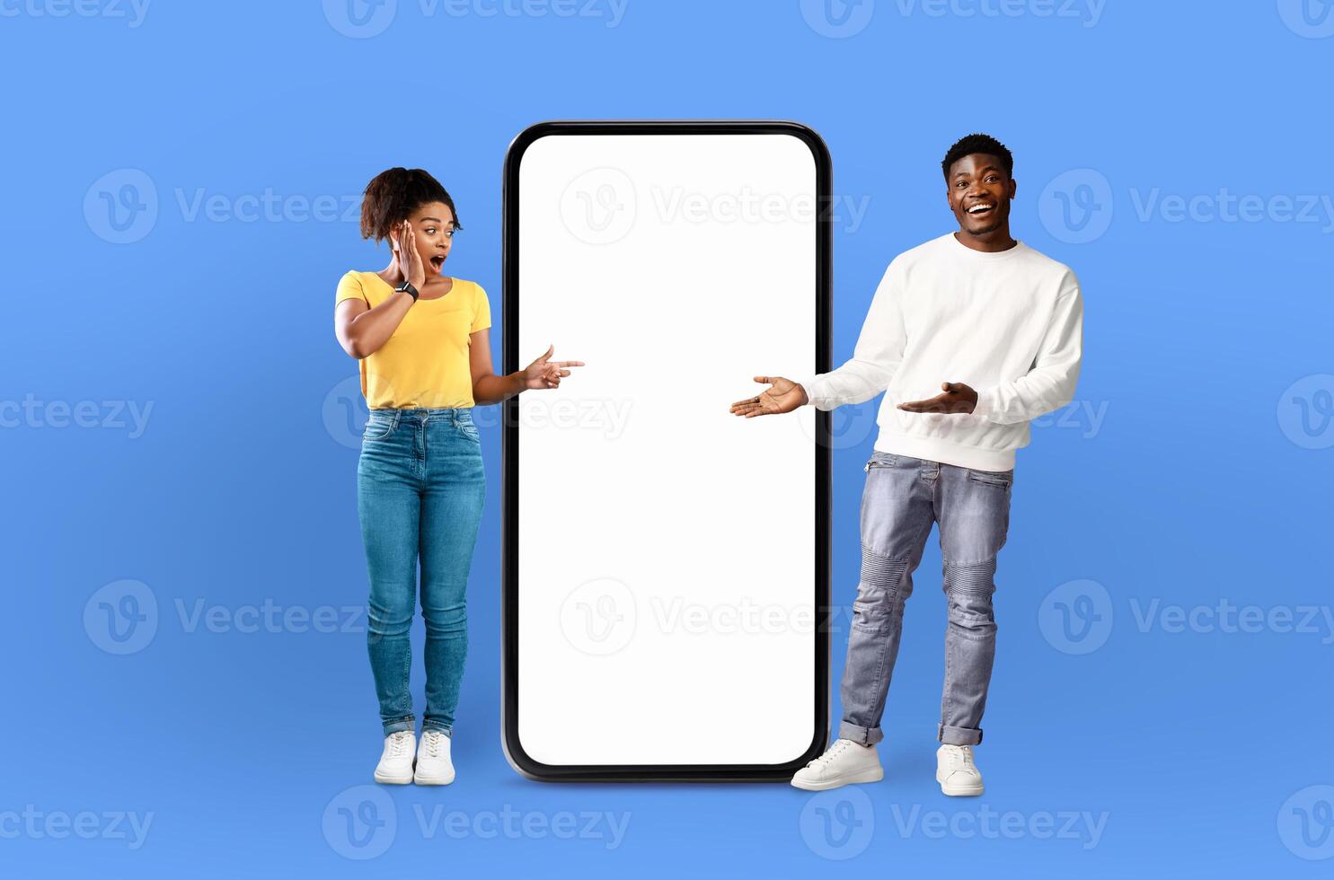 A man and a woman are standing side by side, looking at a blank screen on a phone. The man is holding the phone, while the woman is gesturing towards it with a curious expression. photo