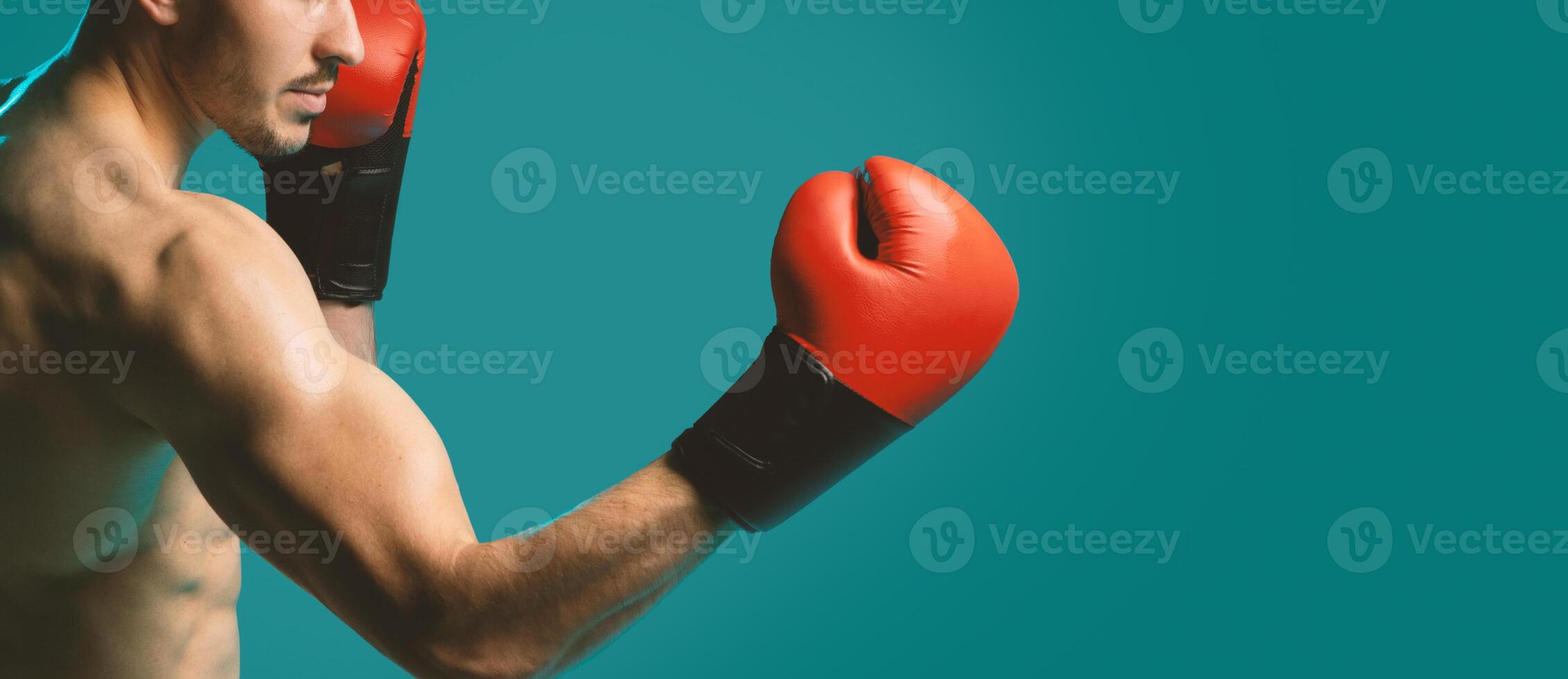 A man wearing boxing gloves strikes a strong and confident pose against a vibrant blue background. His muscles are tense, and he exudes a sense of power and determination, copy space photo