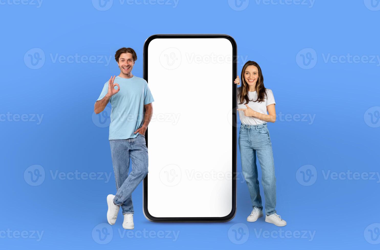Positioned on a striking blue backdrop, the young European man and woman, both beaming, flank a giant smartphone awaiting your personalized content on its screen. photo