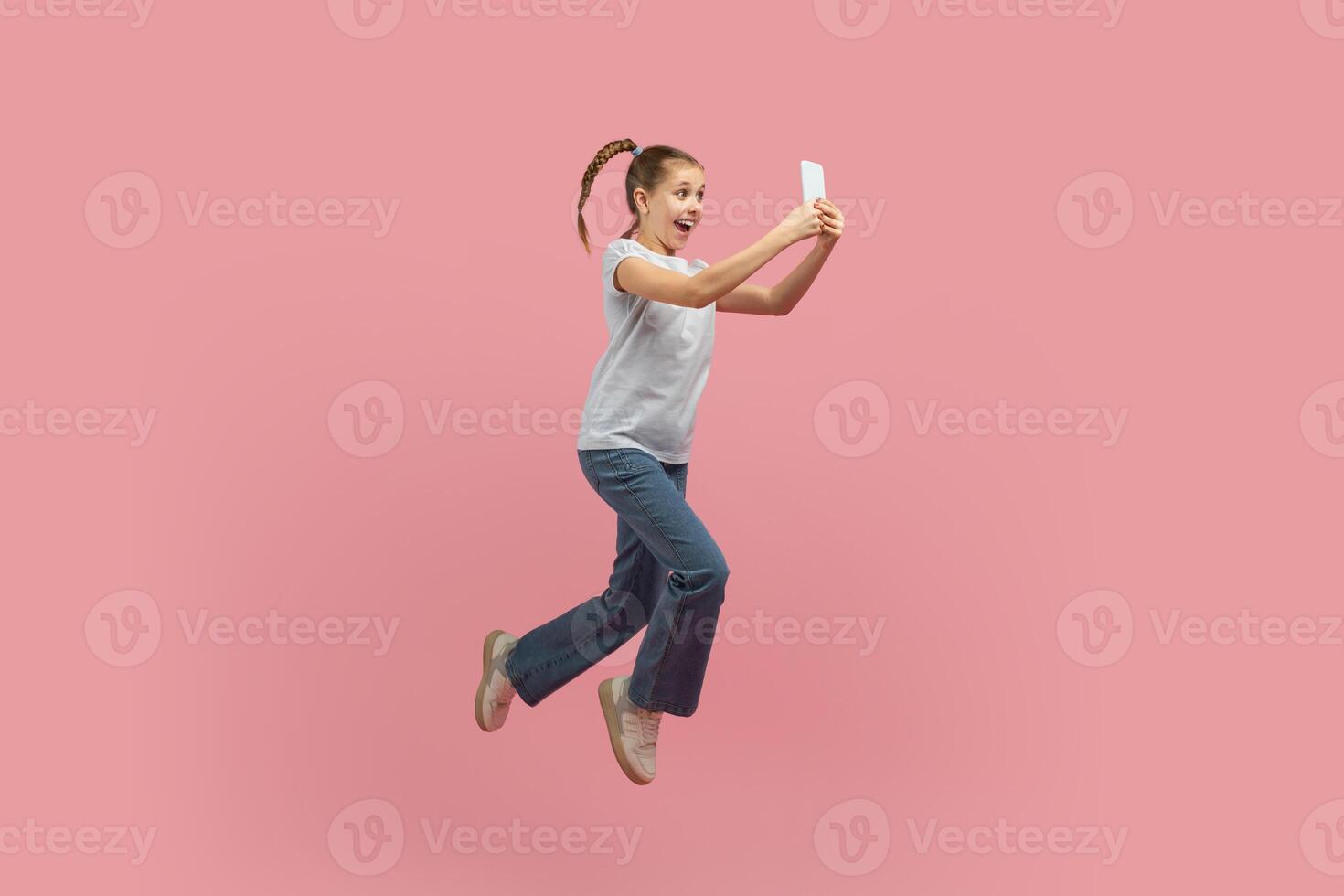 A young girl is captured mid-air, jumping energetically with a cell phone in hand. She appears joyful and carefree as she leaps into the sky with a mobile device. photo