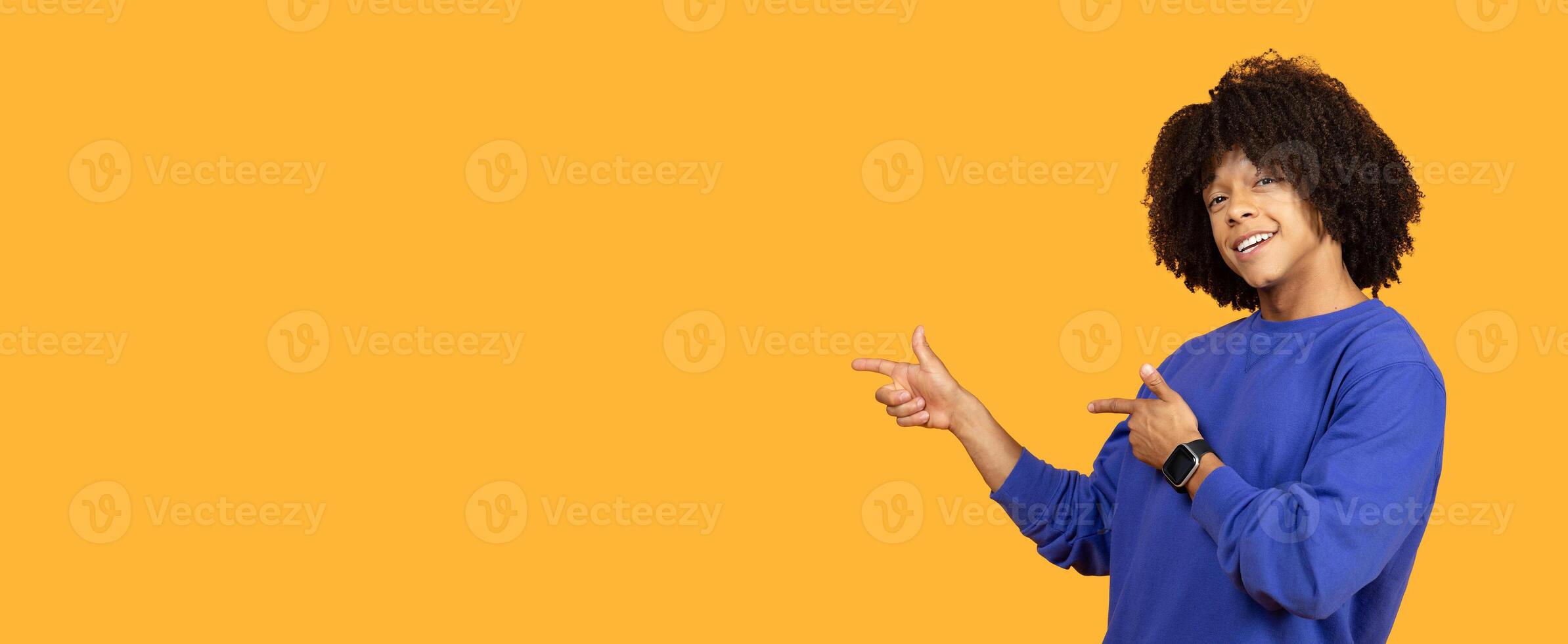 A young man expresses excitement while gesturing playfully pointing at copy space against a vibrant yellow background. photo