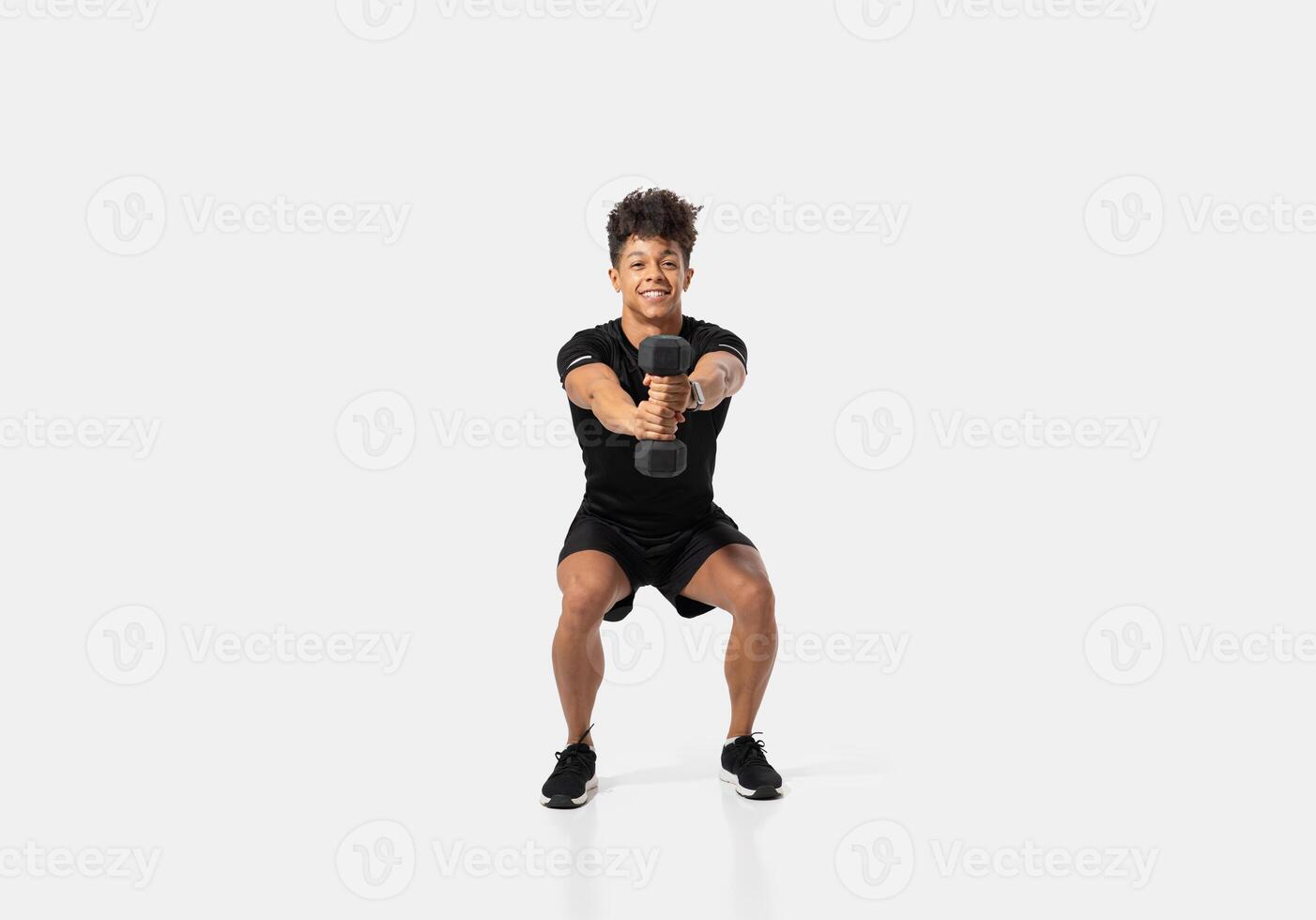 A man is engaged in a squat exercise while holding a dumbbell in each hand. This athletic endeavor takes place in a sleek indoor gym setting with bright ambient lighting photo