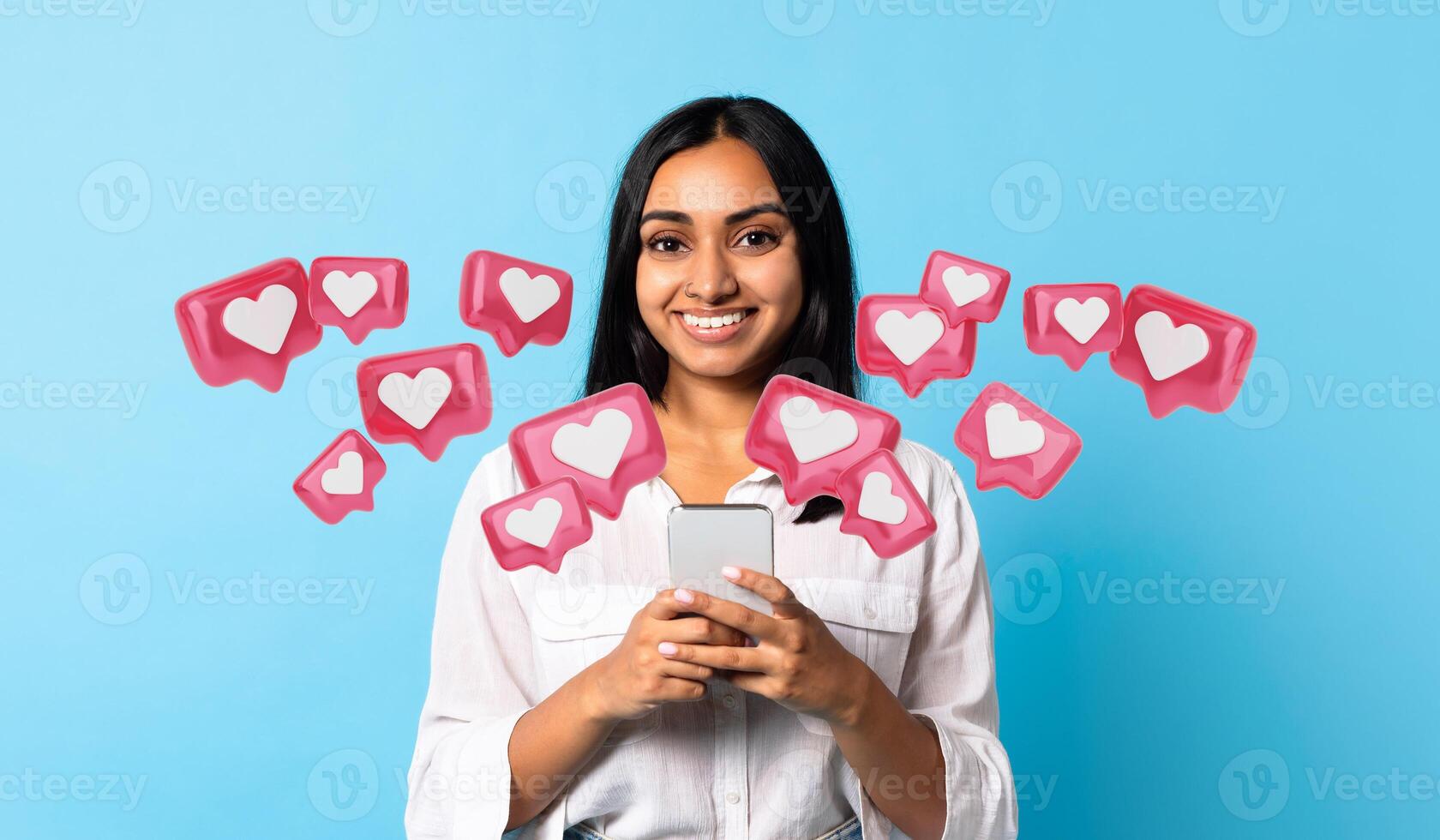 Young Indian woman texting lover on her smartphone against vibrant blue studio, reflecting the age of modern online communication. Happy lady holding cellphone, posing and chatting photo