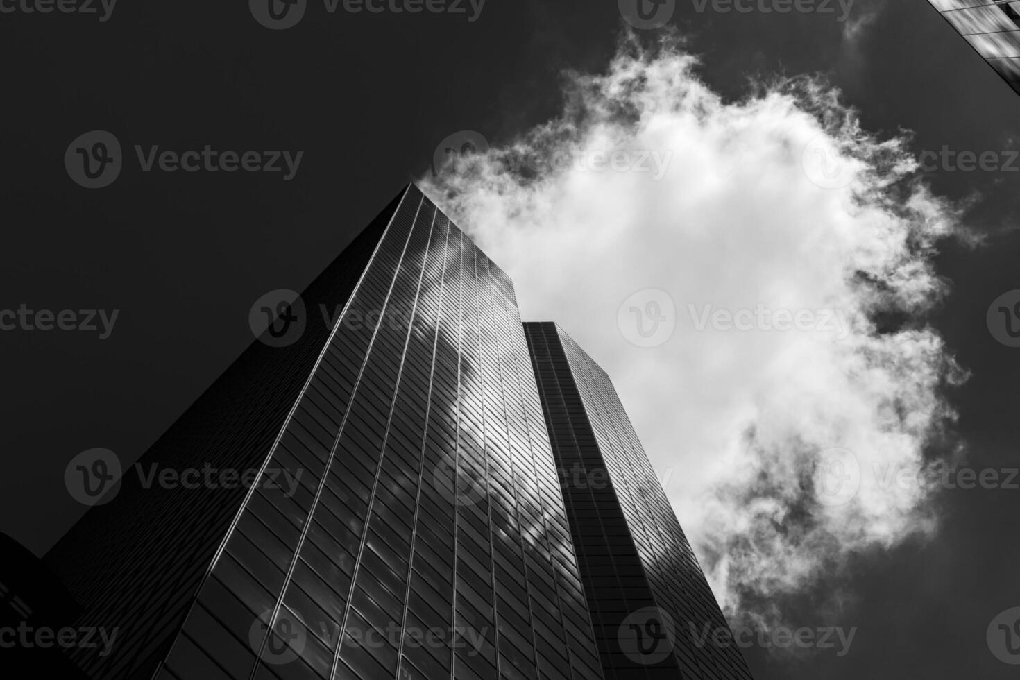Black and white photograph of a tall building with a cloud in the sky photo