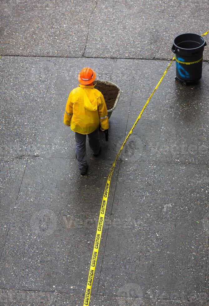 A man in a yellow safety vest and hard hat is walking with a wheelbarrow photo