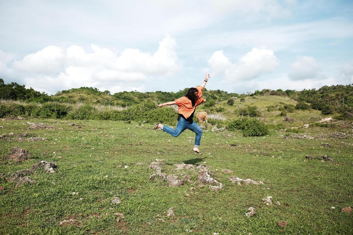 Asian woman is jumping on grass land with cow on the mountain. Young female happy for freedom life and destination travel with tropical wild and nature photo