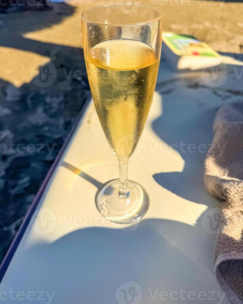 glass of sparkling wine on sun bed with towel and book in the background . High quality photo