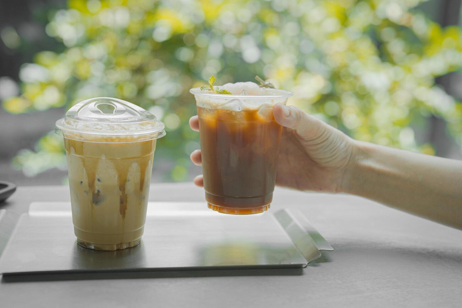 hand of woman holding a take-out iced lychee americano on black table at coffee shop. photo