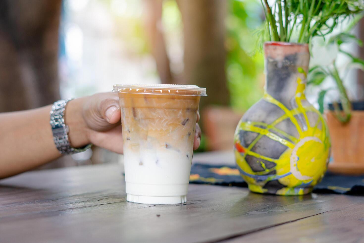 Hand of man holding glass of ice coffee on wooden table. photo
