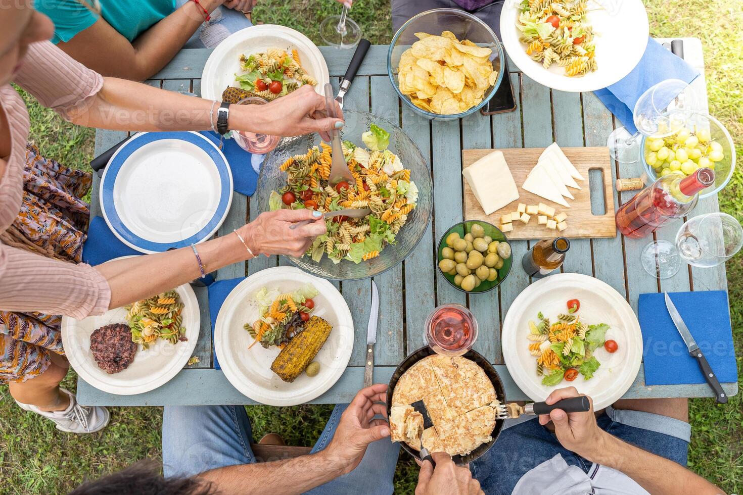 Multicultural family sitting at wooden table having dinner. They have plates full of food and glasses with drinks. photo
