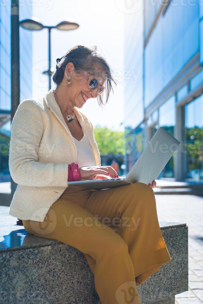 Happy attractive business woman middle-aged working smiling with laptop in front of a modern building. Vertical photo. photo