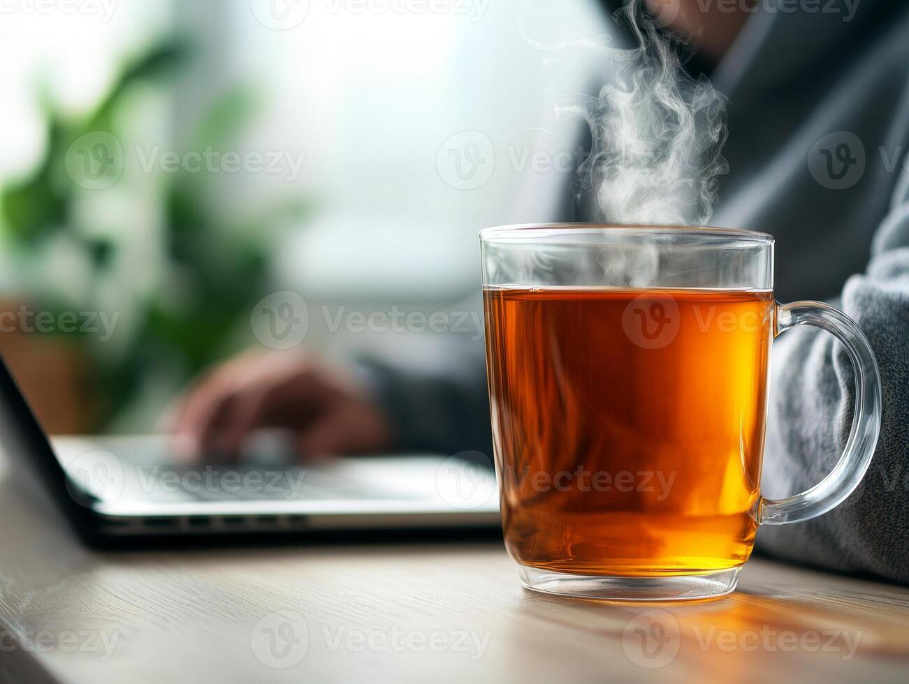 A steaming cup of tea on a desk near a laptop, creating a cozy workspace atmosphere. photo