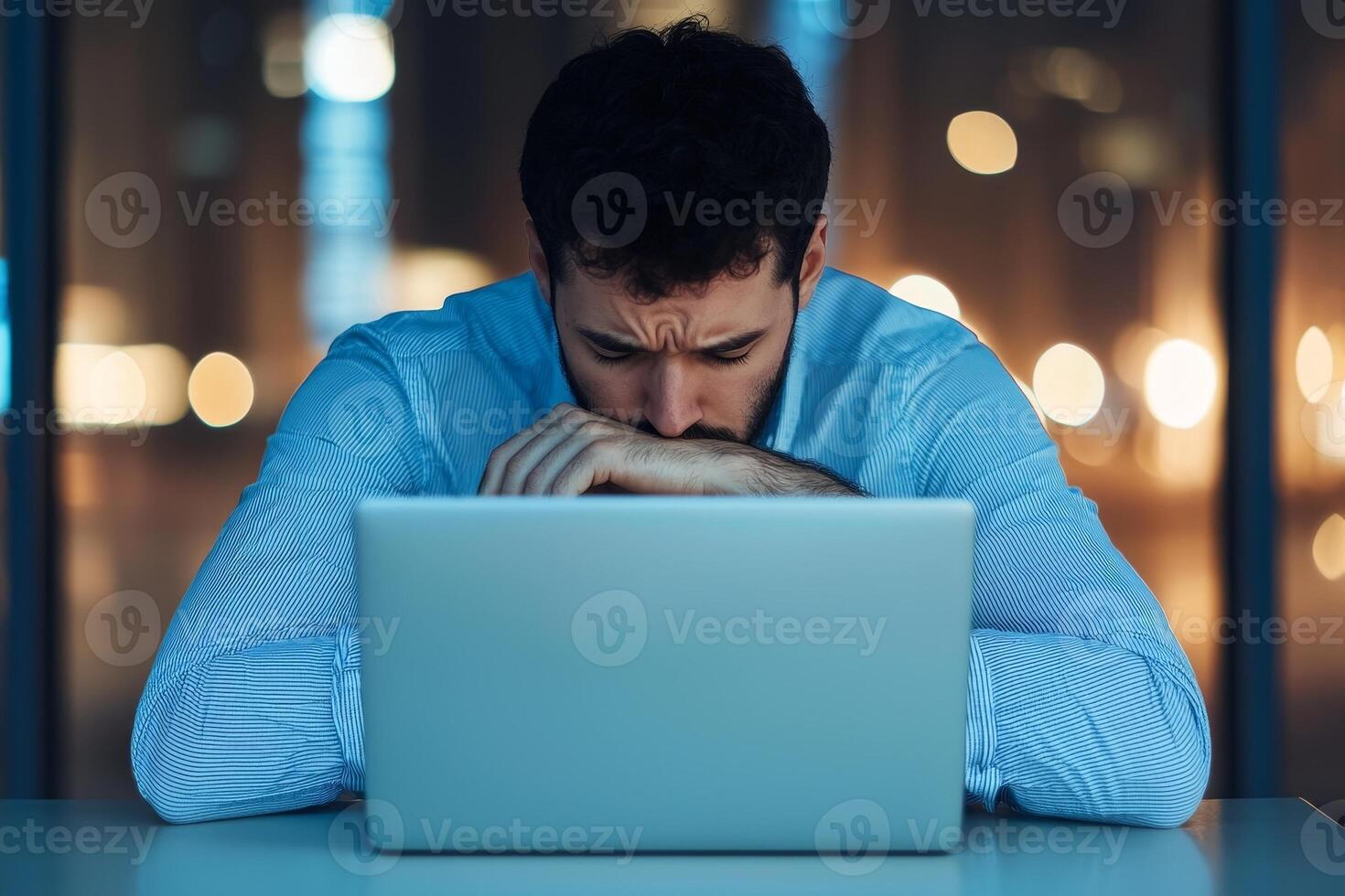 Frustrated man working at laptop in a dimly lit office environment. photo