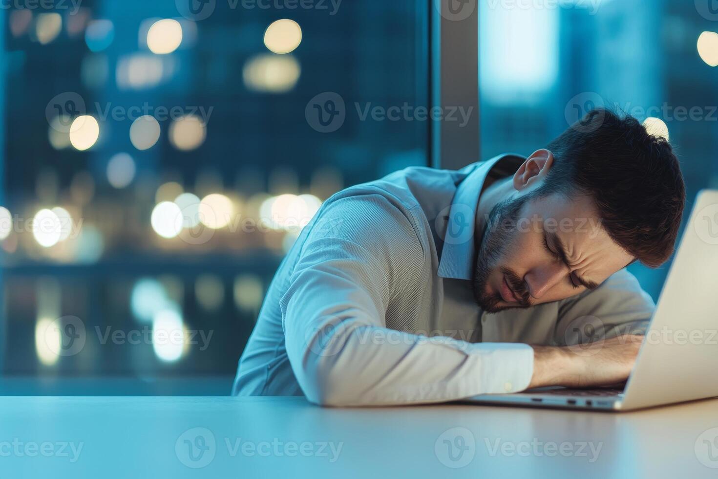 Stressed man resting his head on a laptop at night, soft bokeh background. photo
