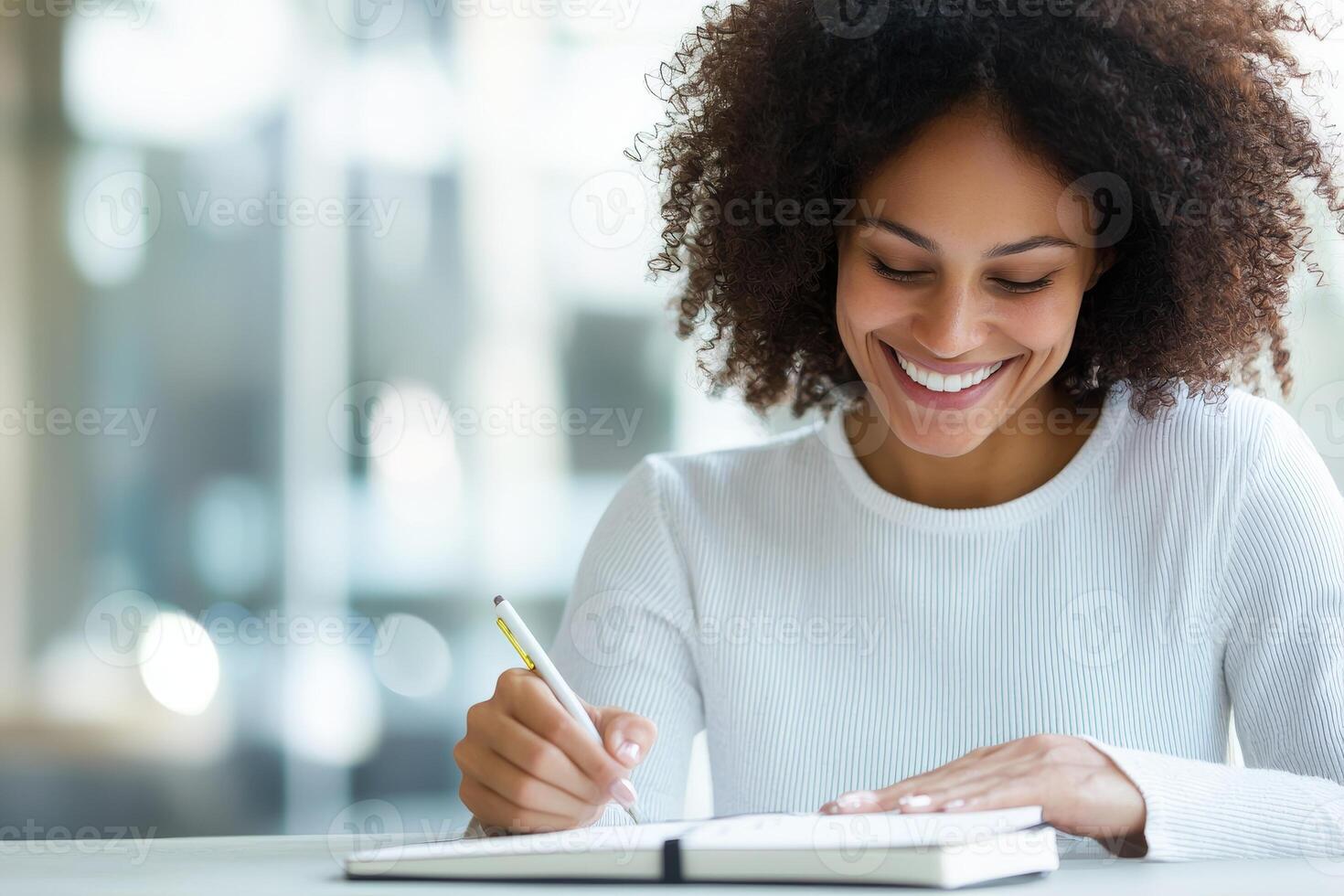 Happy woman writing in notebook, indoor setting, smiling with curly hair. photo