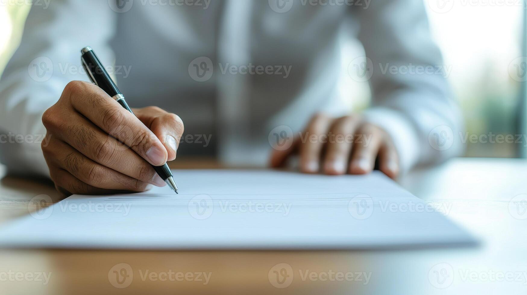 Person writing on a blank sheet of paper with a pen on a wooden table. photo