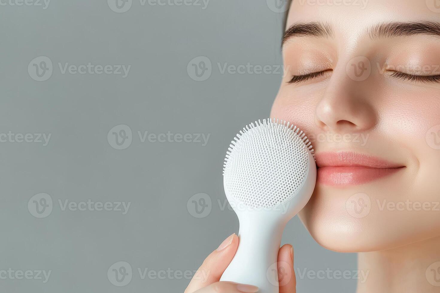 Woman using a facial cleansing device, soft skin, gray background. photo