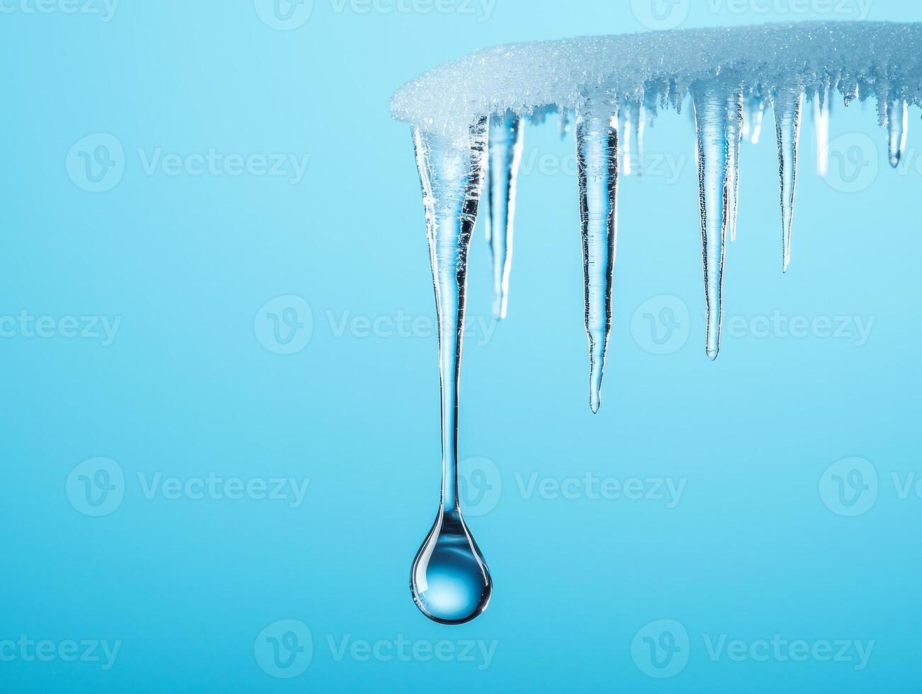 Icicles hanging from a roof against a blue background, water droplet forming beneath. photo