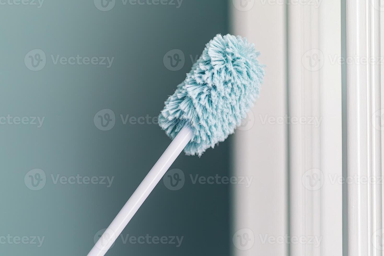 Blue cleaning duster tool against a green wall with soft focus. photo