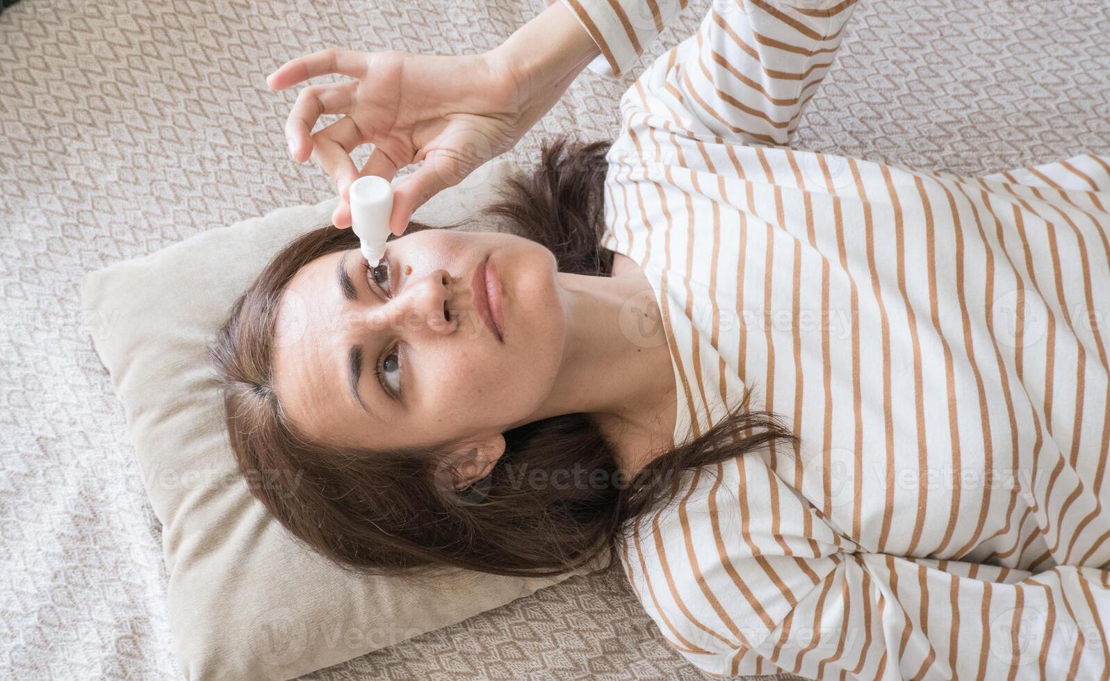 Top view of a woman who drips antibacterial drops into her eyes while lying on the couch photo