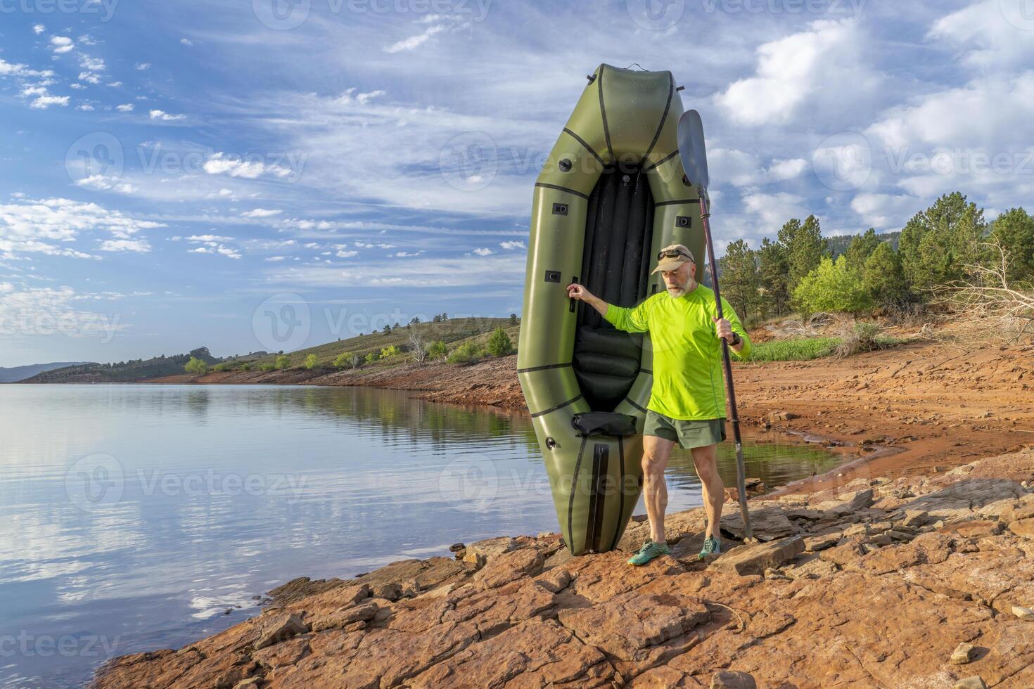 senior male paddler is launching an inflatable packraft on a shore of Horsetooth Reservoir in Colorado photo