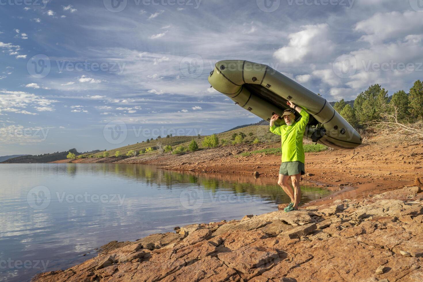 senior male paddler is launching an inflatable packraft on a shore of Horsetooth Reservoir in Colorado photo
