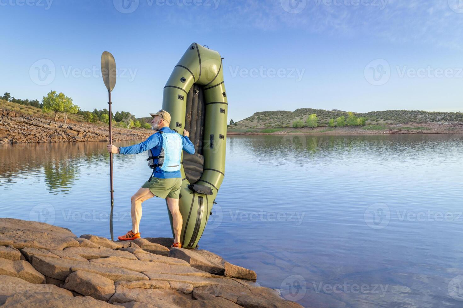 senior male paddler is launching an inflatable packraft on a shore of Horsetooth Reservoir in Colorado photo