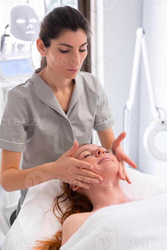 Therapist massaging face of relaxed woman in cosmetology clinic photo