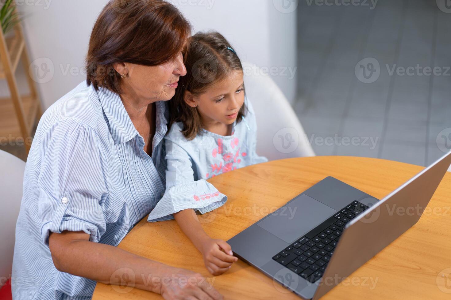 From above of granddaughter and grandmother using laptop on table photo