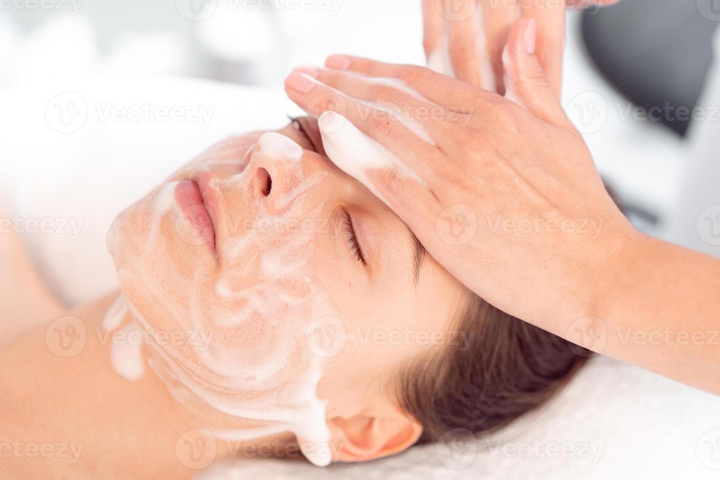 Therapist massaging woman's face with cream at cosmetology salon photo