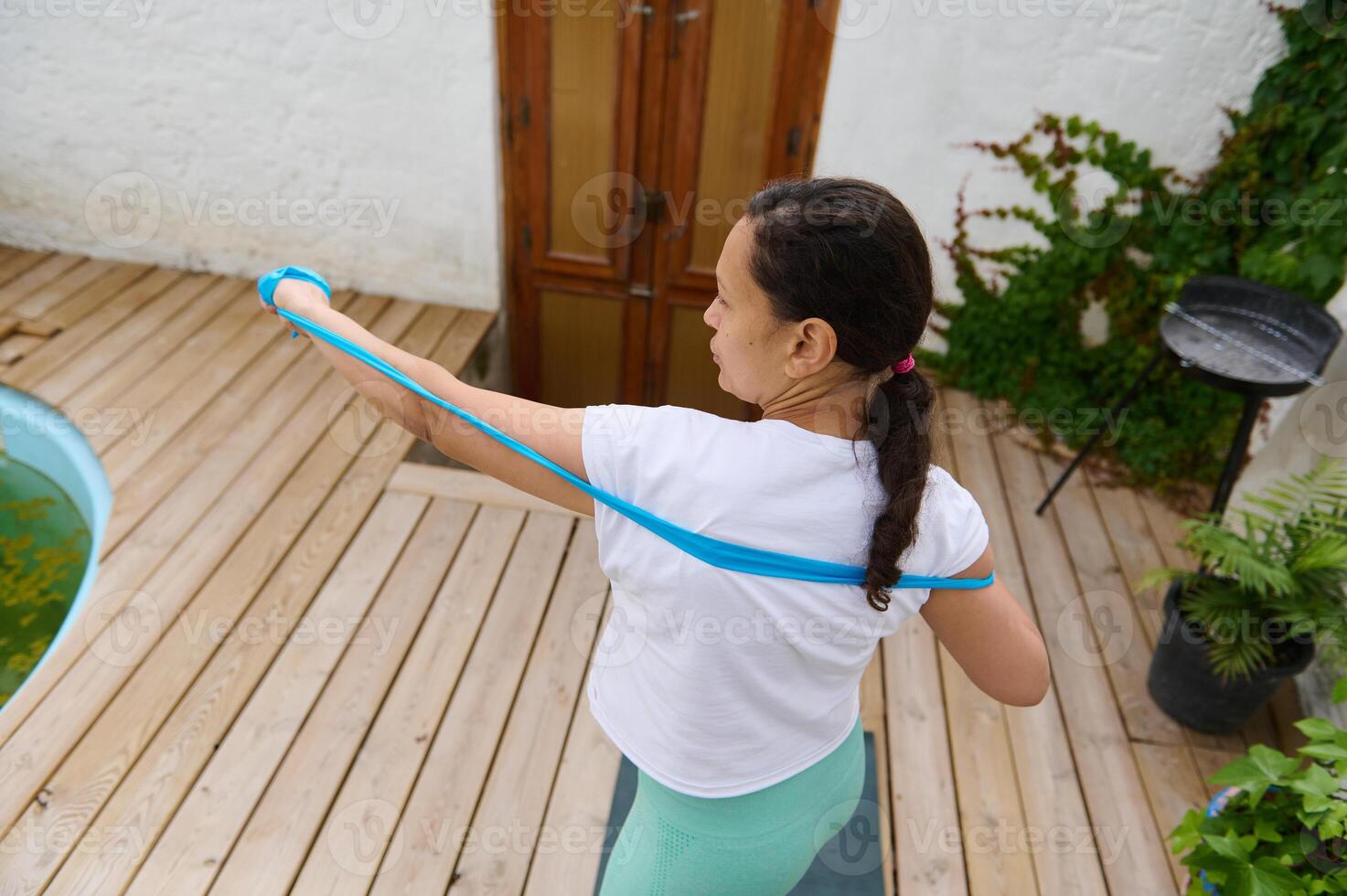 Woman exercising with resistance band on wooden deck for a home workout, promoting fitness and healthy lifestyle photo