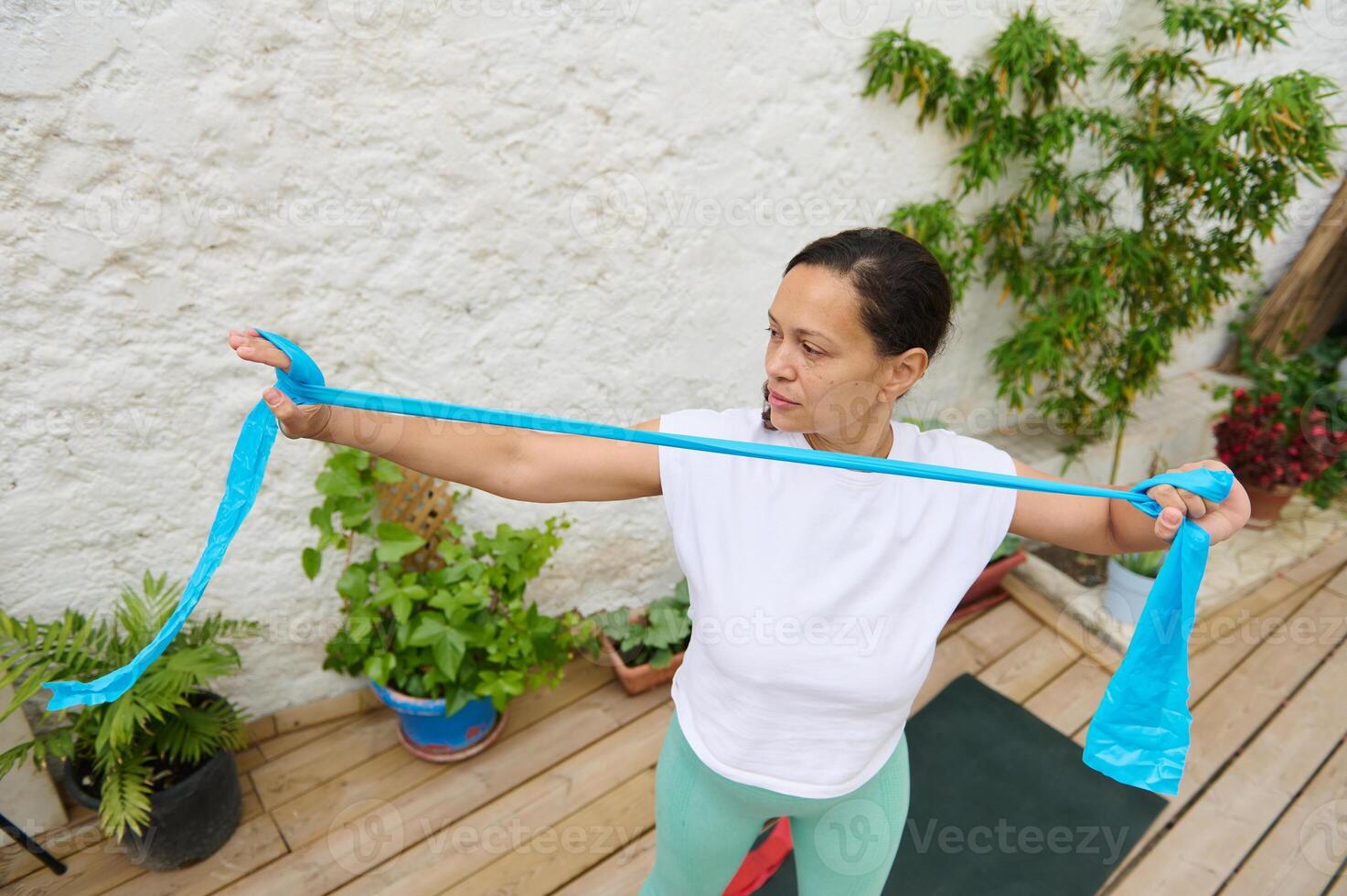 Woman exercising with resistance band outdoors in a peaceful garden setting, focusing on strength training and fitness for a healthy lifestyle photo