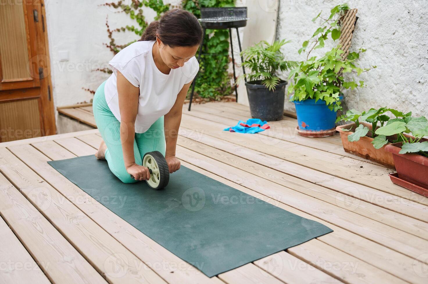 Woman practicing ab exercises with a wheel roller on a yoga mat in an outdoor setting on a wooden deck photo
