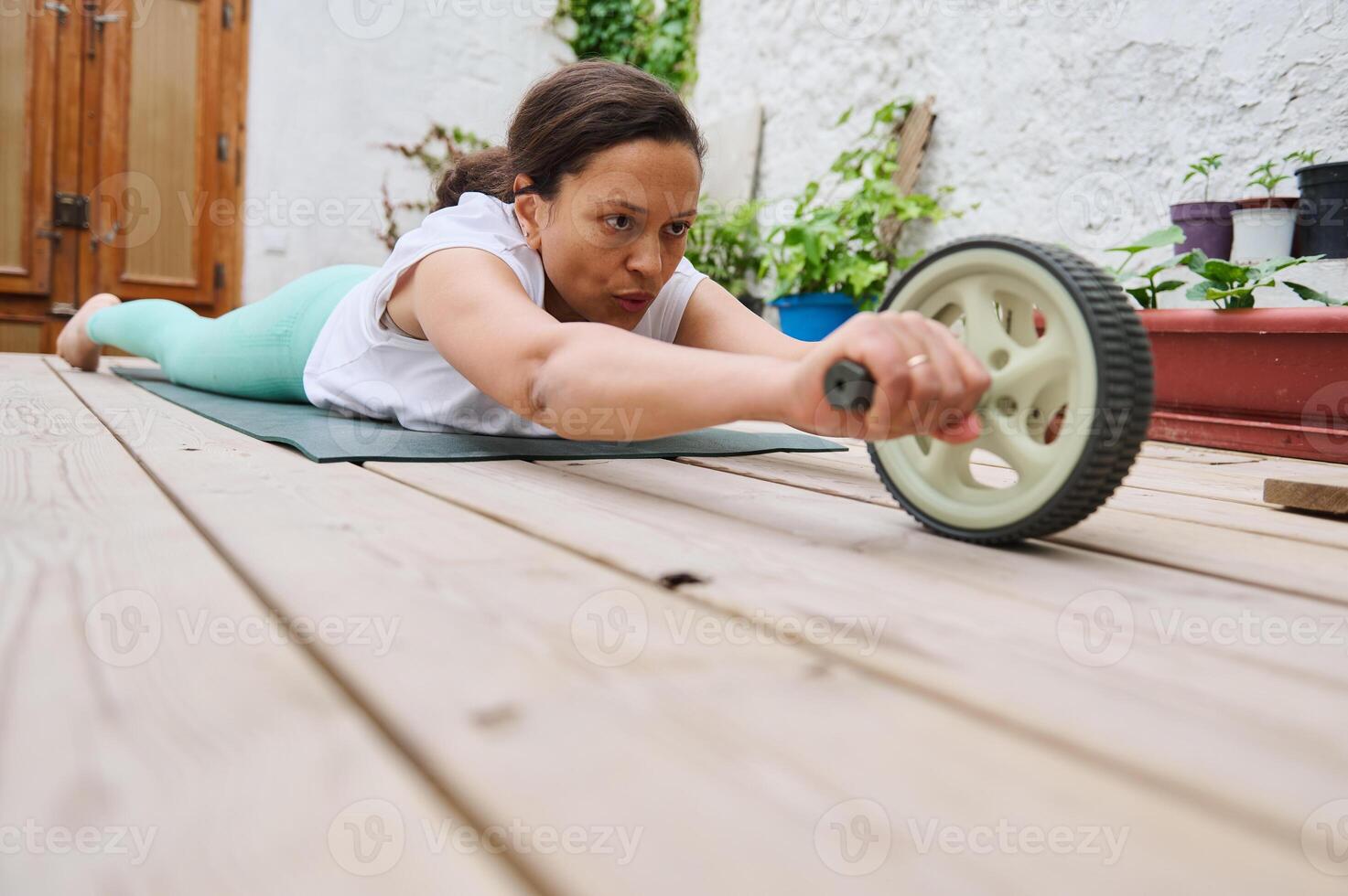 Determined woman exercising with an ab roller on a yoga mat in an outdoor setting, showing strength and concentration photo
