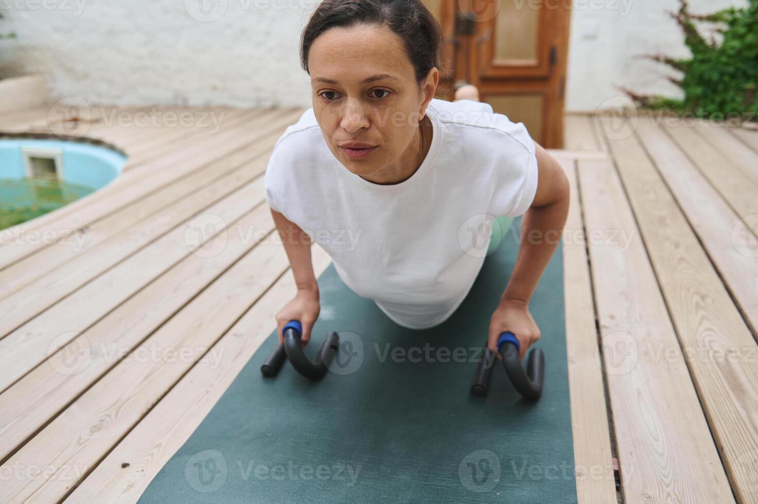 Woman engaging in outdoor push-up exercise with push-up bars on a wooden deck, focusing on upper body strength and fitness. photo