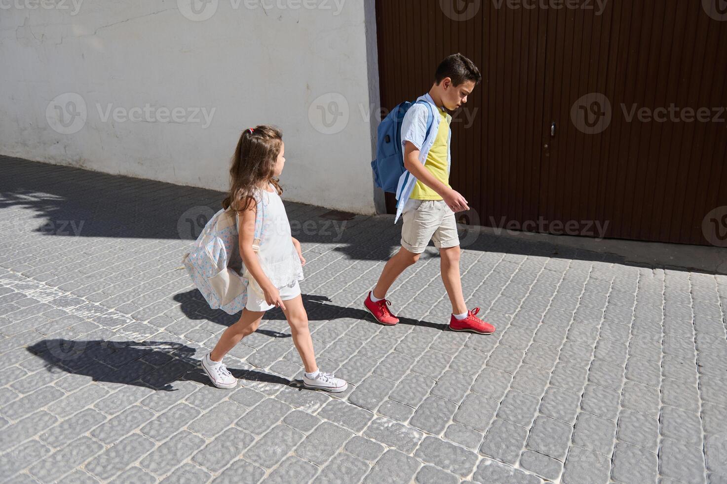 Two children walking to school with backpacks on a sunny day photo