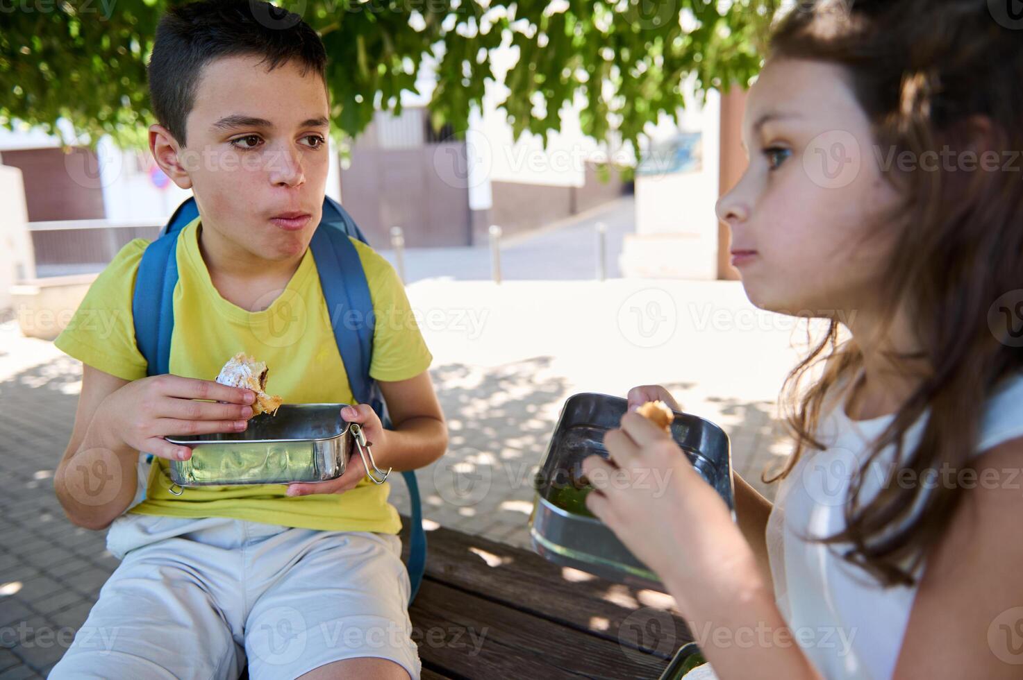 Children enjoying lunch outdoors with lunchboxes under tree shade photo