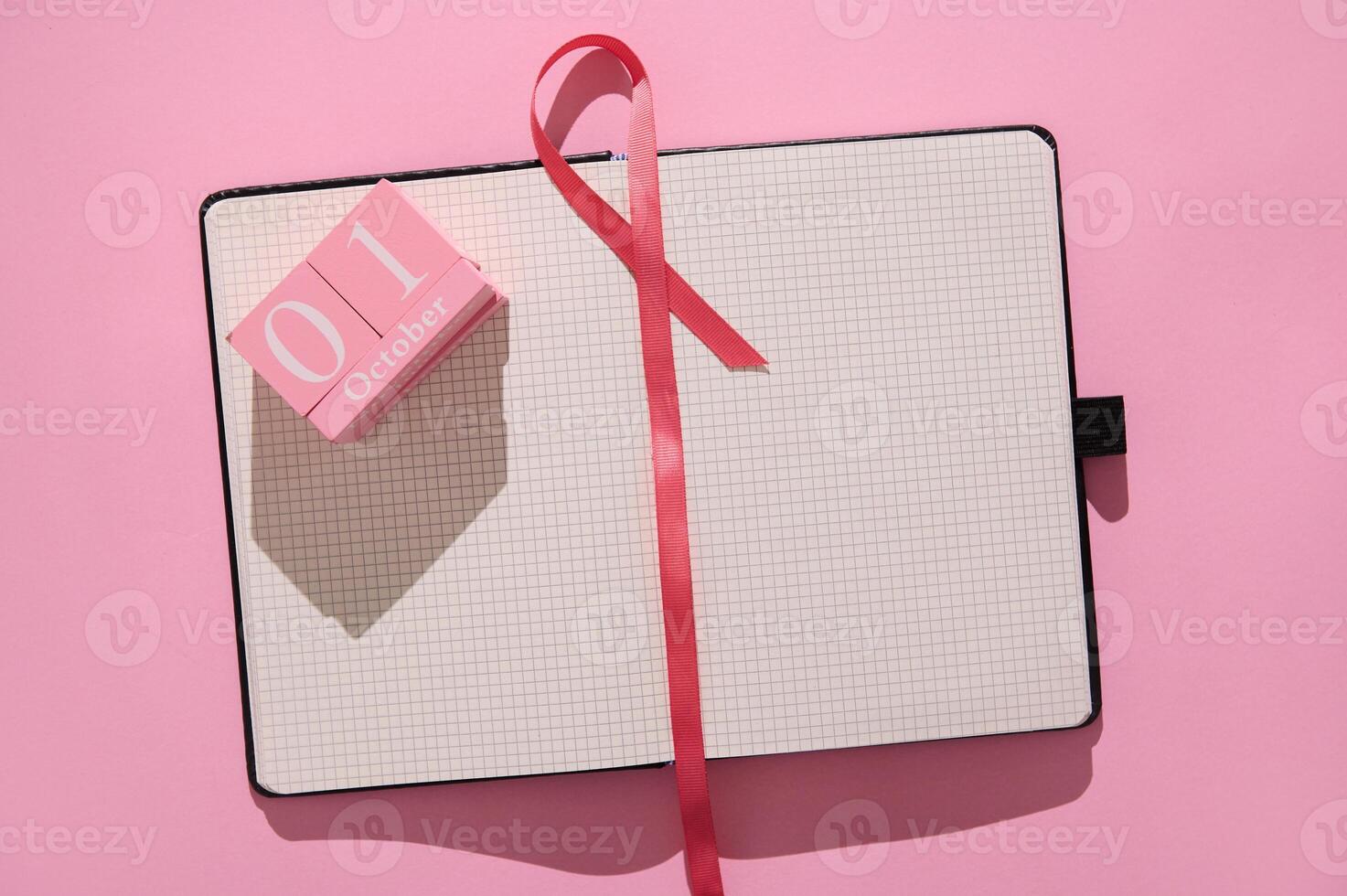 Open notebook with pink ribbon and October 1st calendar block on pink background photo