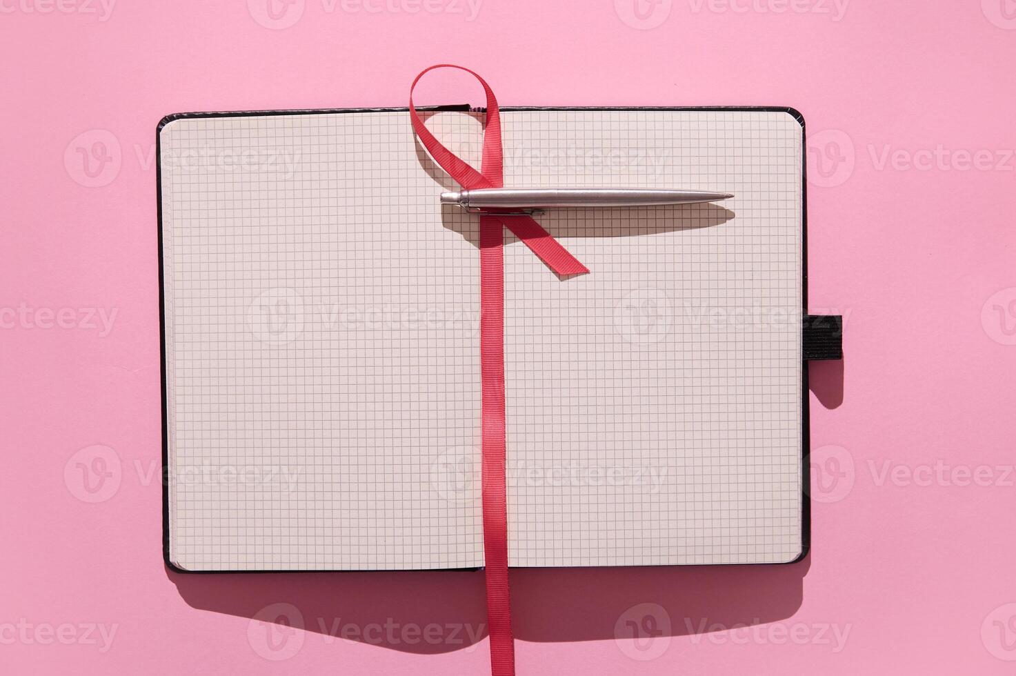 Open notebook with grid pages and pen on vibrant pink background with red ribbon bookmark photo