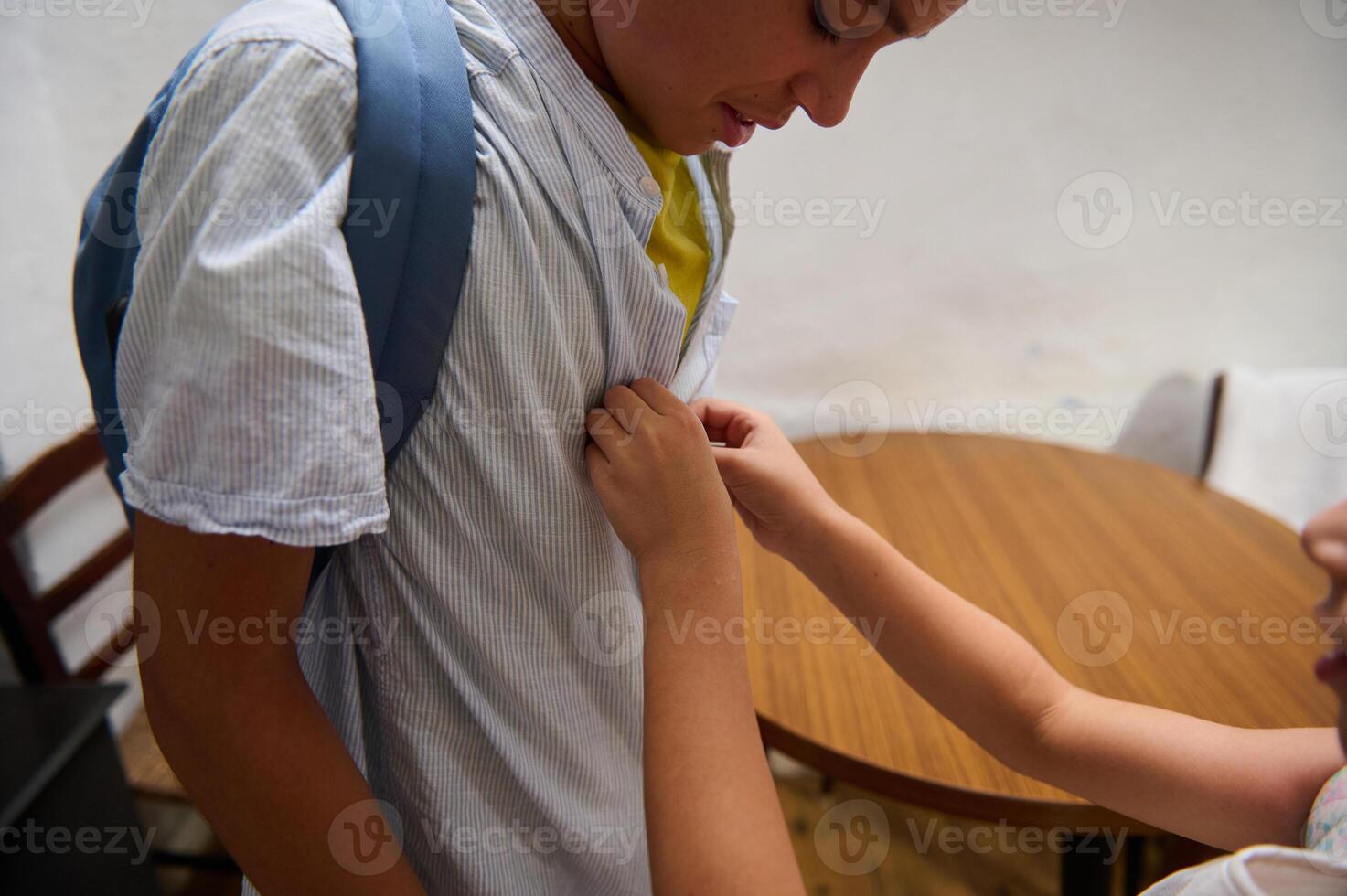 Child helping a peer with a school backpack indoors photo
