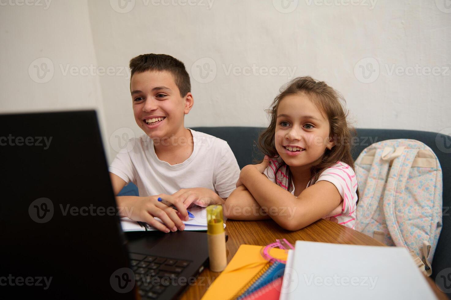 Smiling children enjoying online learning with a laptop at home photo