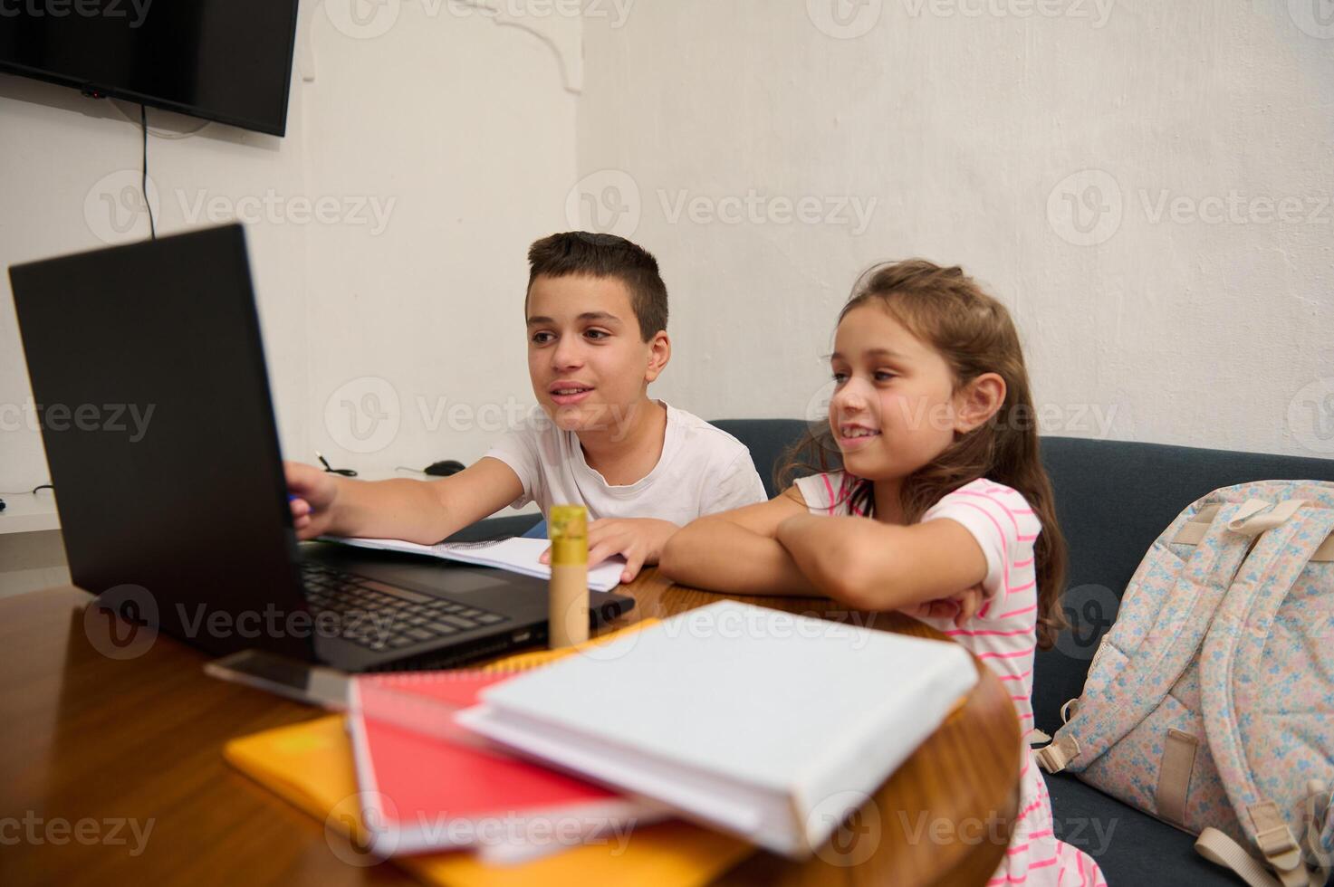 Children learning on laptop at home surrounded by books photo