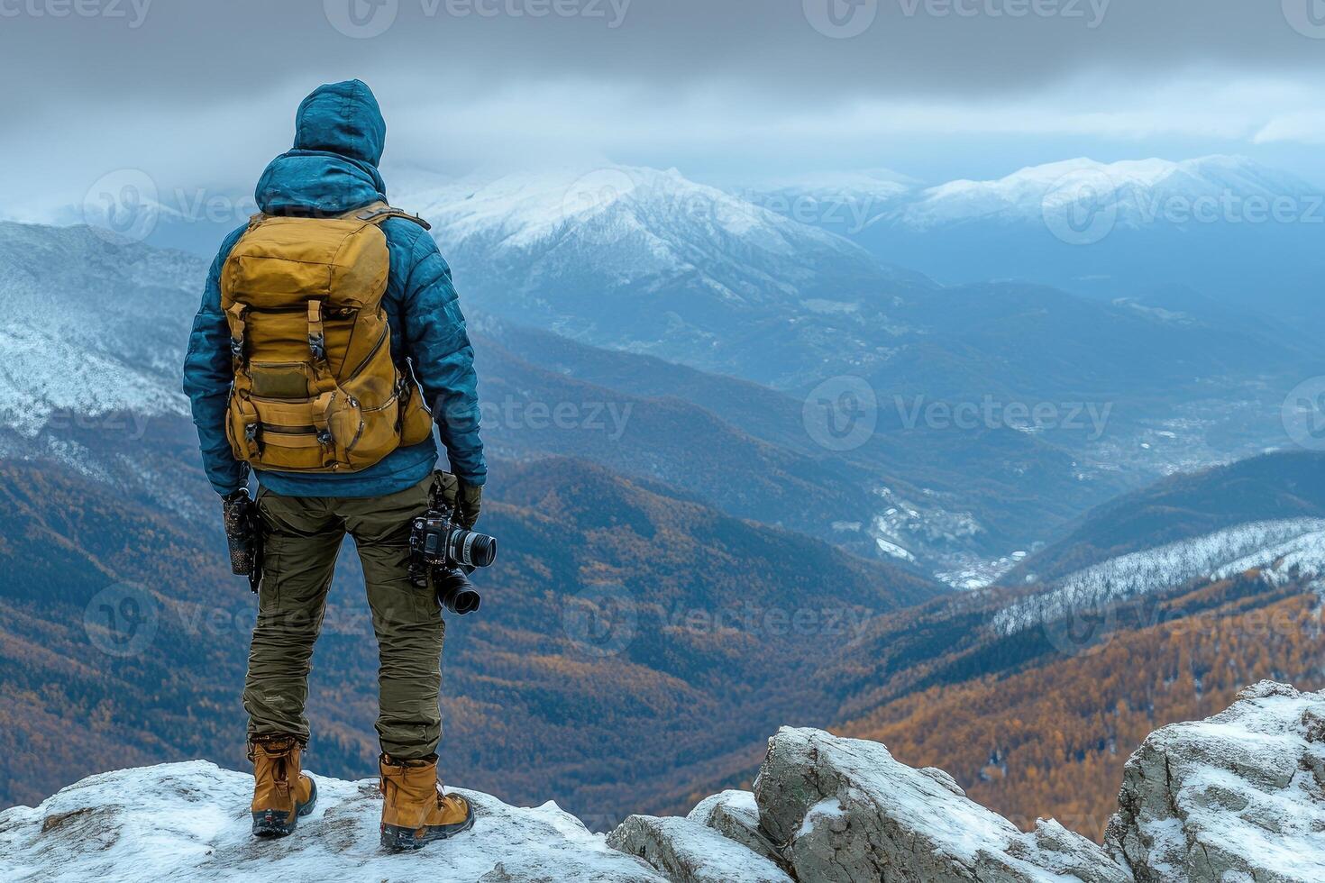 A Photographer Standing on a Snowy Mountain Peak Overlooking a Valley photo