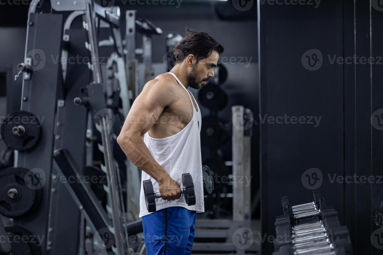 Muscular sport man is practice weight training on double dumbbells for biceps and triceps muscle inside gym with dark background for exercising and workout photo