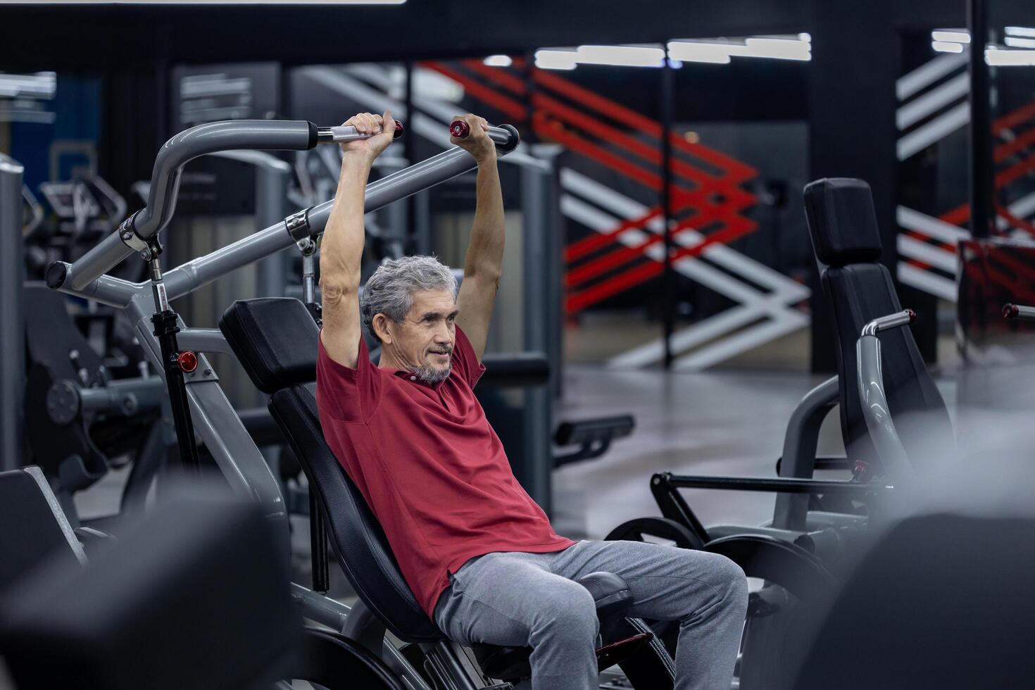 An asian senior man in sportswear doing weight lifting the machine to gain bicep and back muscle while having exercise training in the gym for longevity and retirement concept photo
