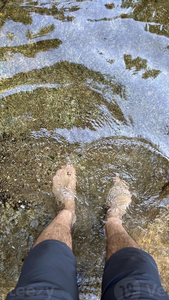 Male feet without shoes, barefoot, tourist's feet in cold mountain water, without shoes, first person view photo