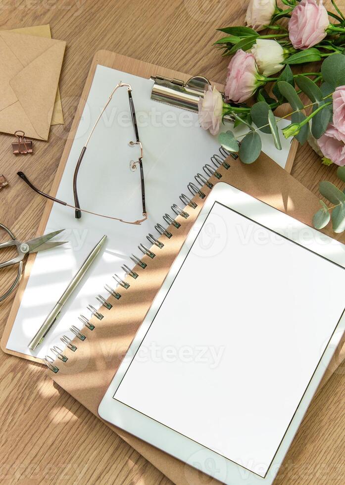 Stationery workspace with a blank tablet, notebook, and flowers on a wooden table, perfect for creative planning in natural light photo