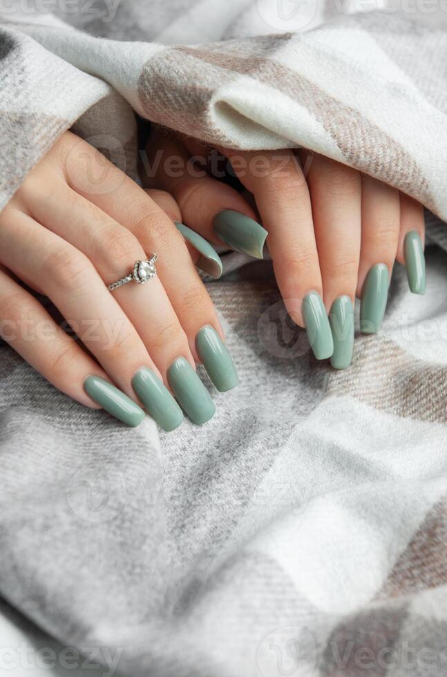 Elegant mint green manicure on long nails adorned with a ring, wrapped in a cozy blanket during a relaxing indoor moment photo