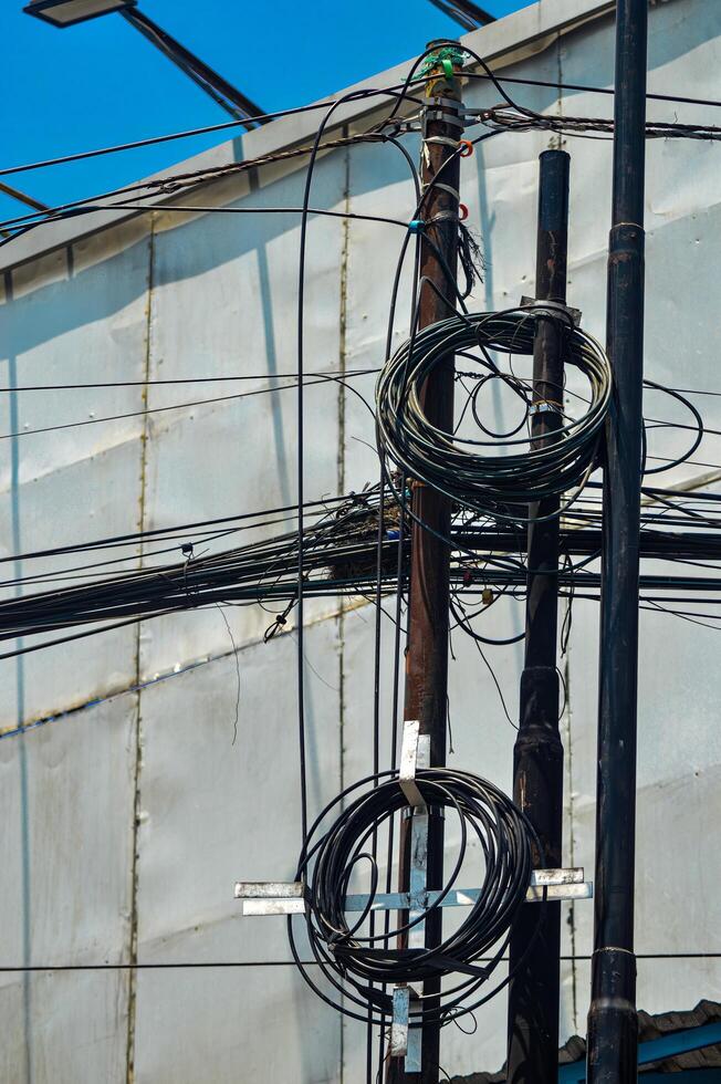 Urban chaos depicted through tangled electrical wires against a building and clear blue sky, showcasing complex city infrastructure photo